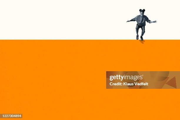 full length of young woman jumping from orange wall - regarder vers le bas photos et images de collection