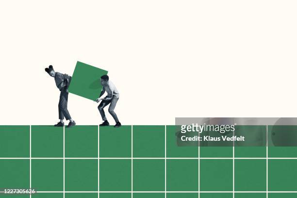 woman and man carrying large green block on grid - sostegno morale foto e immagini stock