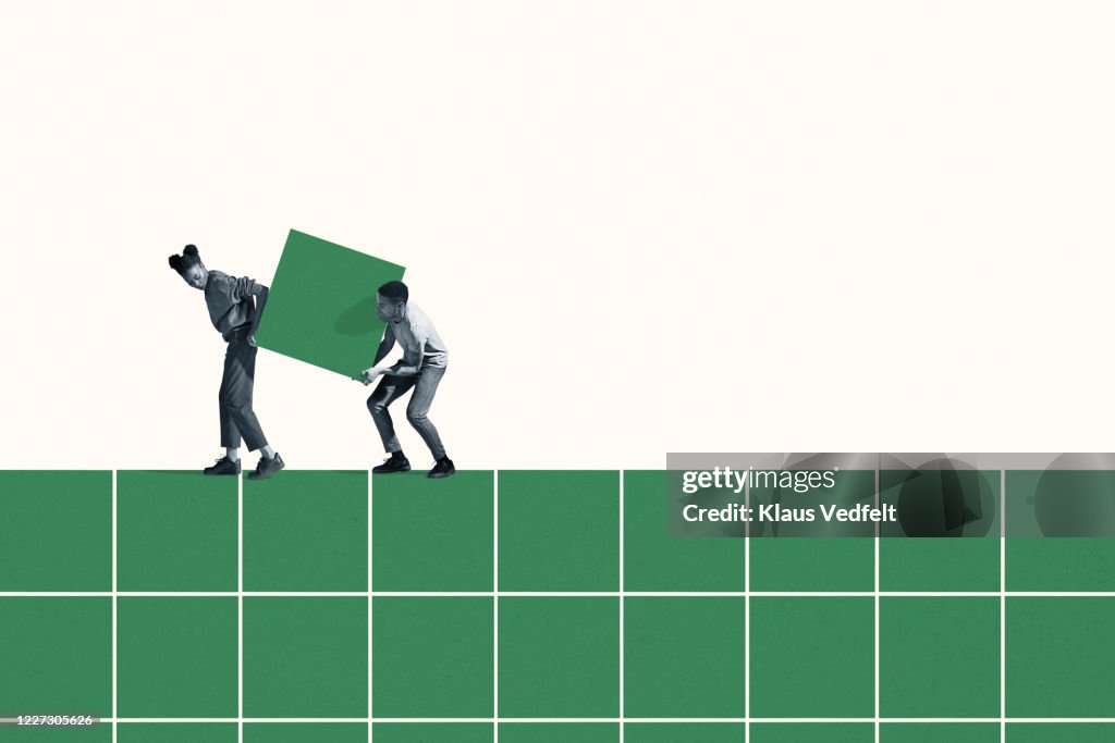 Woman and man carrying large green block on grid