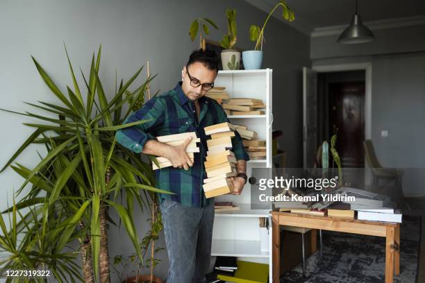 uomo millenario che organizza le sue collezioni di libri - arrangiare foto e immagini stock