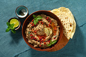 homemade spread of baked eggplant baba ganoush in a bowl with pomegranate seeds, lime, olive oil and lime slices on a blue linen tablecloth with flat bread