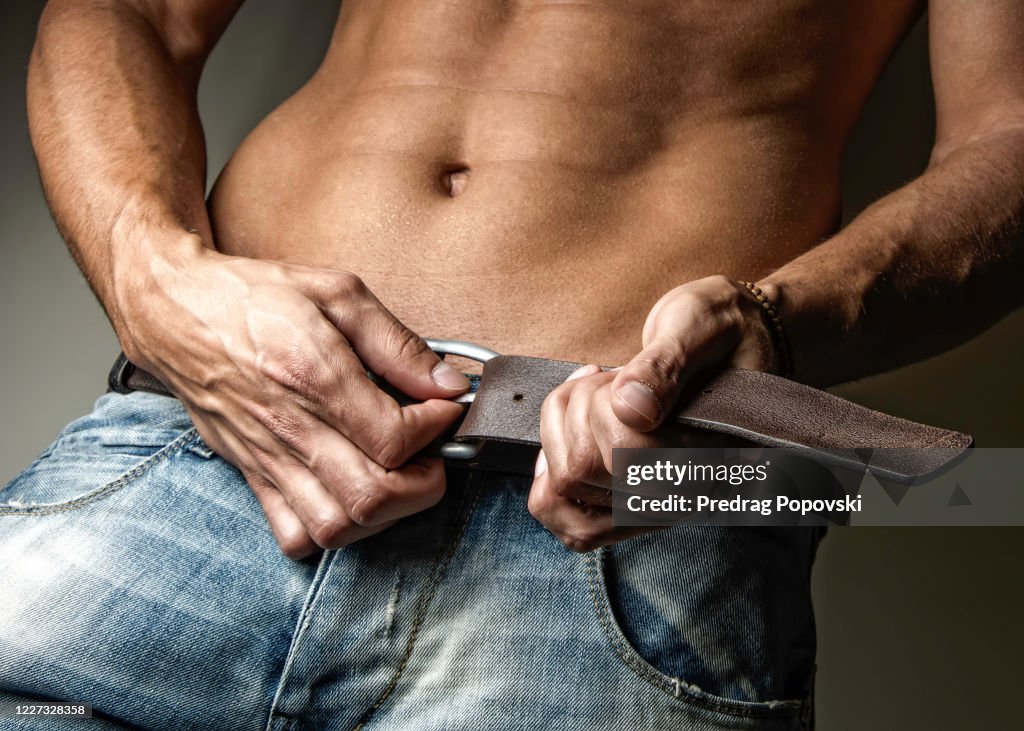Young handsome man undoing his belt and jeans