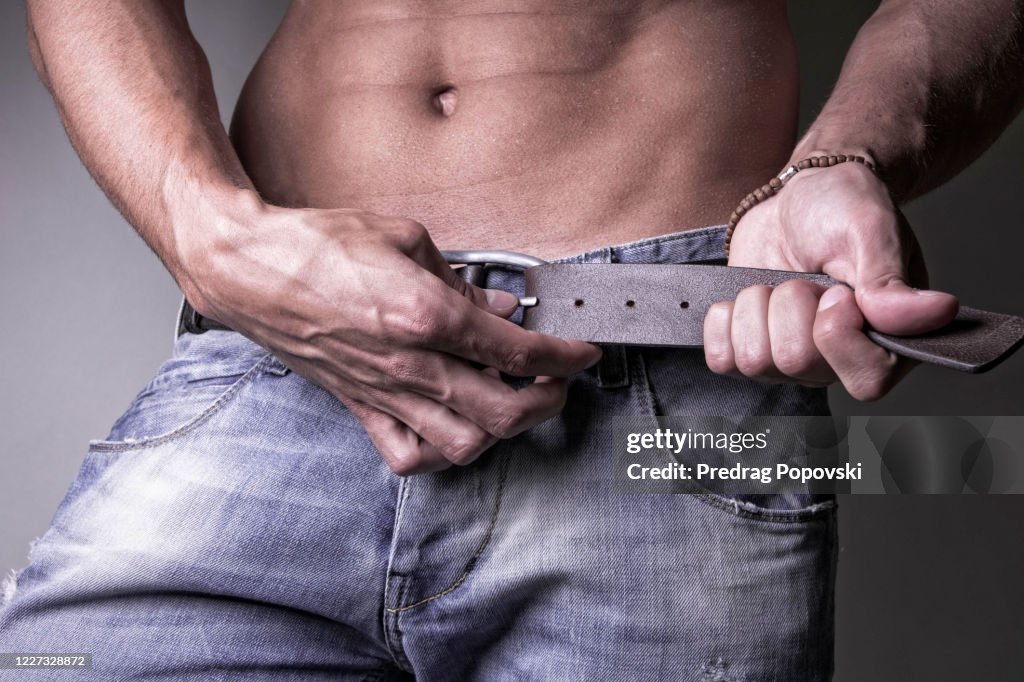 Young handsome man undoing his belt and jeans