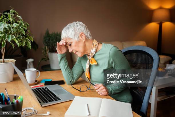 mature woman working indoors at home - makeshift desk stock pictures, royalty-free photos & images