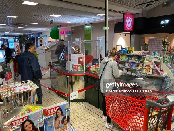 Caissière protégée par un film plastique et consommatrice avec un masque pour se protéger contre le Covid-19 lors du passage en caisse au supermarché...