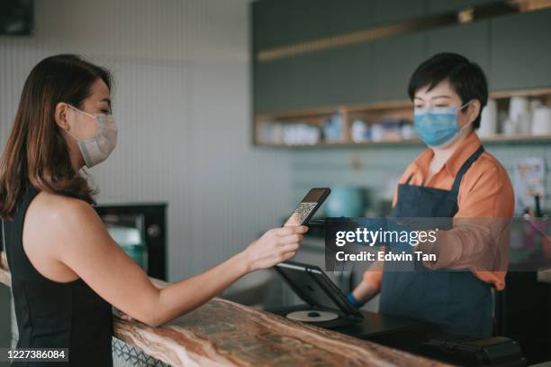 eine asiatische chinesische café-besitzerin, die die zahlung von ihrem kunden am schalter mit qr-code kontaktloses bezahlen erhält - die neue normalität stock-fotos und bilder