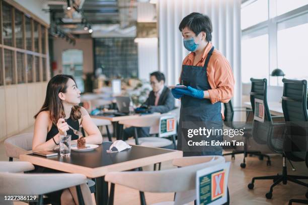 an asian chinese small business cafe owner woman talking to her customer for ordering in the cafe with new normal social distancing standard operating procedure - chinese waiter stock pictures, royalty-free photos & images