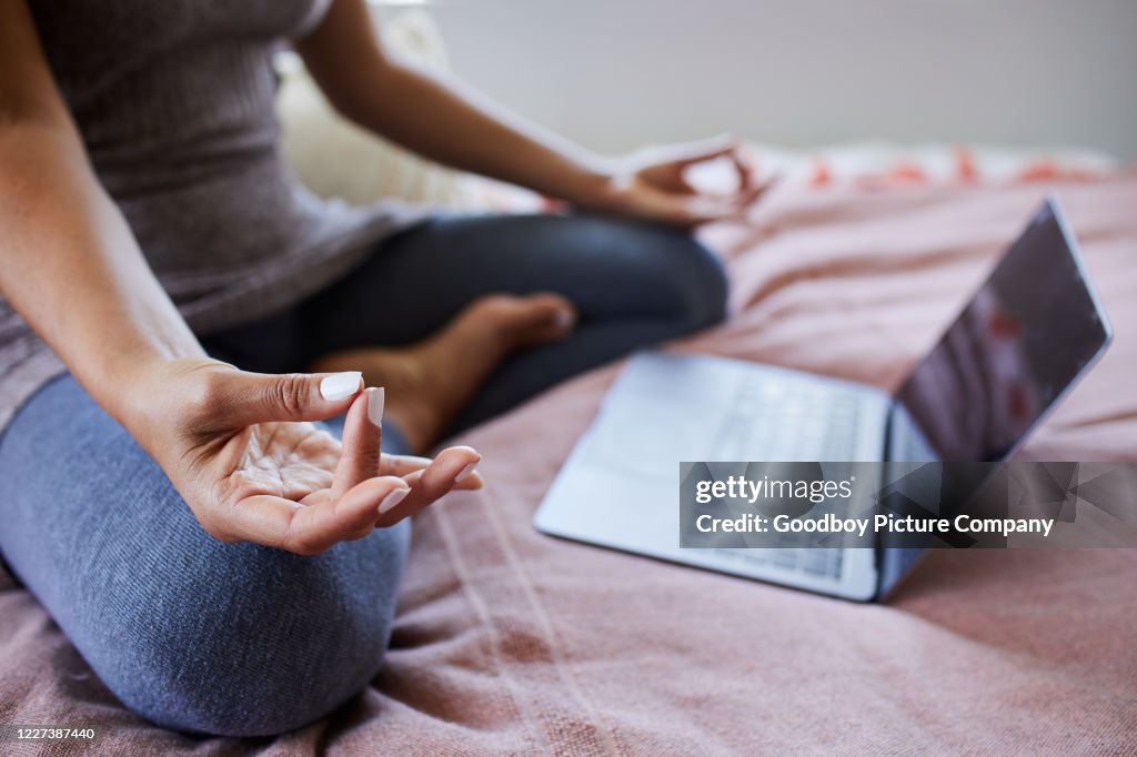 De zitting van de vrouw op haar bed dat een online meditatieklasse streamt