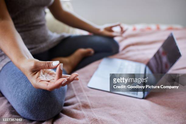 de zitting van de vrouw op haar bed dat een online meditatieklasse streamt - computer work life balance stockfoto's en -beelden