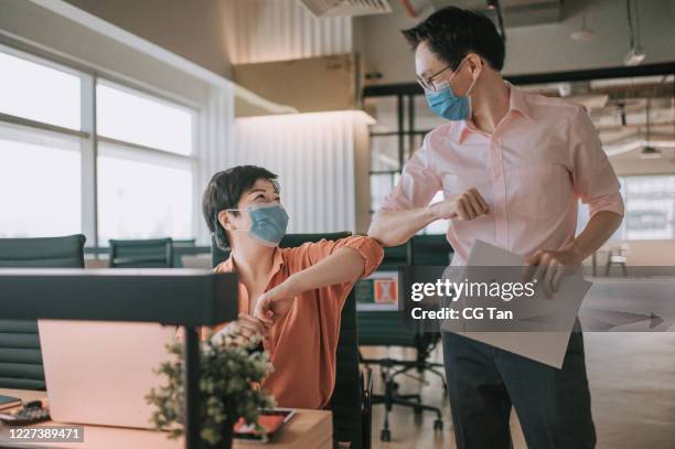 2 asiatische chinesische kollegen grüße über einander mit neuen handshake-stil im büro mit schutzmaske auf - die neue normalität stock-fotos und bilder