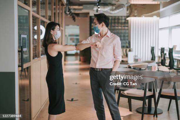 2 asiatische chinesische kollegen grüße über einander mit neuen handshake-stil im büro mit schutzmaske auf - die neue normalität stock-fotos und bilder