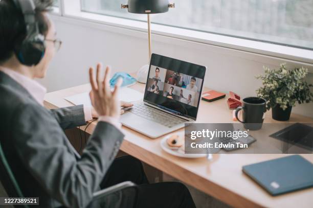 een aziatische chinese midden volwassen zakenman die videoconferentie met zijn collega en bedrijfspartners in het bureau heeft gebruikend hoofdtelefoon en laptop - business meeting chinese stockfoto's en -beelden