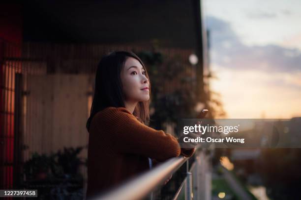 young woman using smartphone on the balcony at sunset - balcony ストックフォトと画像