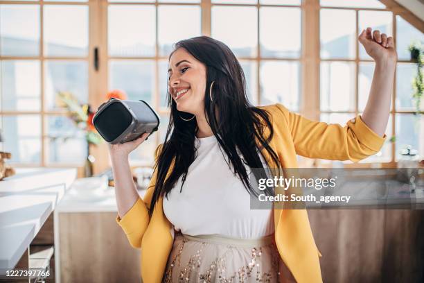 donna che canta e balla a casa e tiene in mano l'altoparlante bluetooth wireless - altoparlante foto e immagini stock