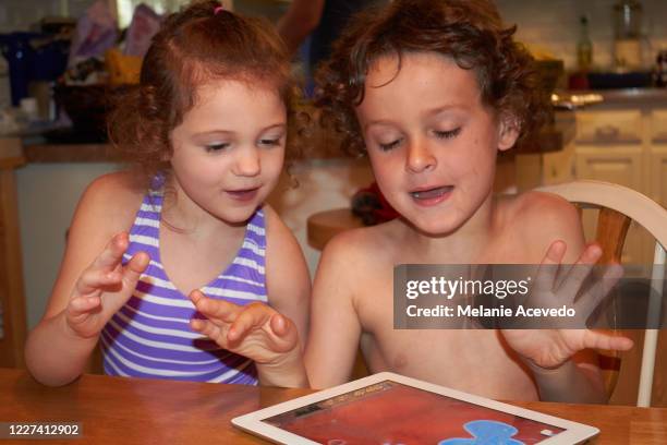 close up shot of a little boy and girl sitting at a kitchen table playing together on a digital tablet. - melanie cousins stock-fotos und bilder