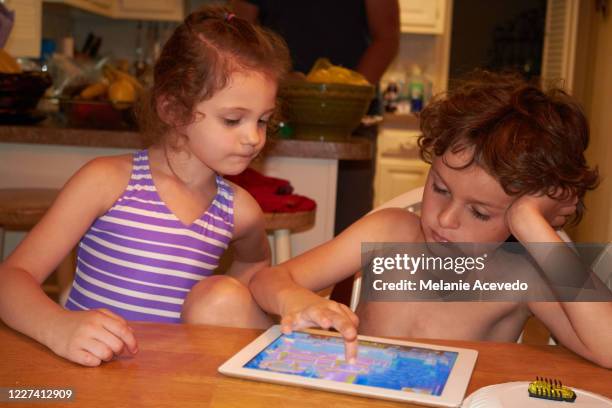 close up shot of a little boy and girl sitting at a kitchen table playing together on a digital tablet. - melanie cousins stock pictures, royalty-free photos & images