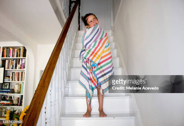 Little boy standing on his stairs in his house wrapped in a striped towel and making a funny face.