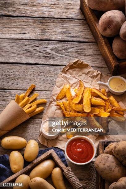french fries potatoes on a rustic wooden board table with raw potatoes around - cone shape stock pictures, royalty-free photos & images