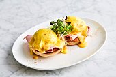 eggs Benedict with arugula, bacon and hollandaise sauce on gray wooden background.
