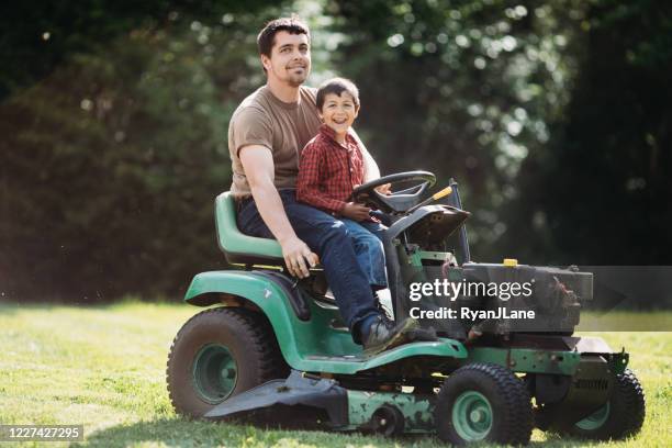 father and son smile on riding mower - father and son gardening stock pictures, royalty-free photos & images