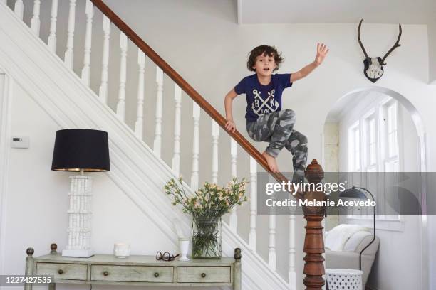 young boy standing on top of stair railing balancing on top of the wooden railing looking at the camera wearing blue graphic design shirt and camouflage pants looking at camera full length view - carly simon signs copies of boys in the trees stockfoto's en -beelden