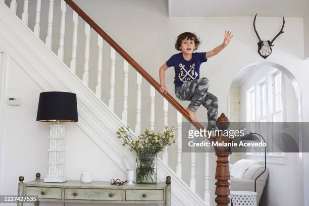 young boy standing on top of stair railing balancing on top of the wooden railing looking at the camera wearing blue graphic design shirt and camouflage pants looking at camera full length view - 玩耍式打鬧 個照片及圖片檔