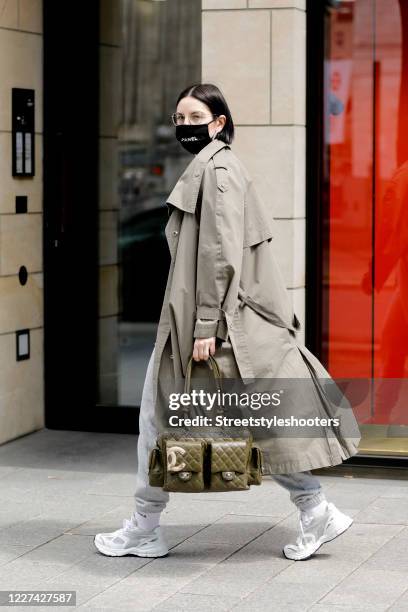 Influencer Maria Barteczko, wearing a black logo face mask by 2nd Couture, a green trenchcoat by The Frankie Shop, a grey basic shirt by H&M, white...