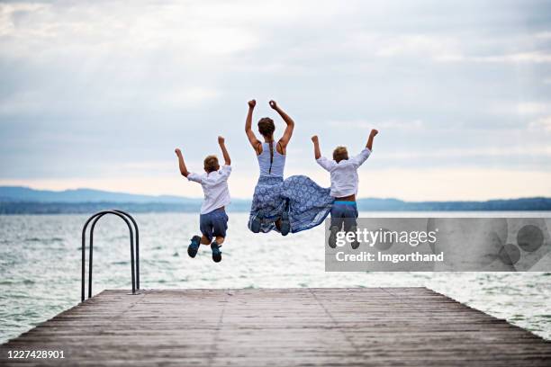niños felices saltando desde el muelle del lago - sirmione fotografías e imágenes de stock