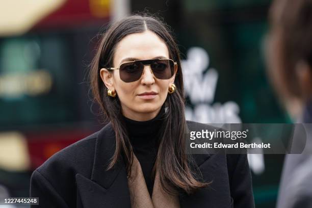Guest wears sunglasses, earrings, a black turtleneck, a camel jacket, a black oversized coat, outside Ann Demeulemeester, during Paris Fashion Week -...