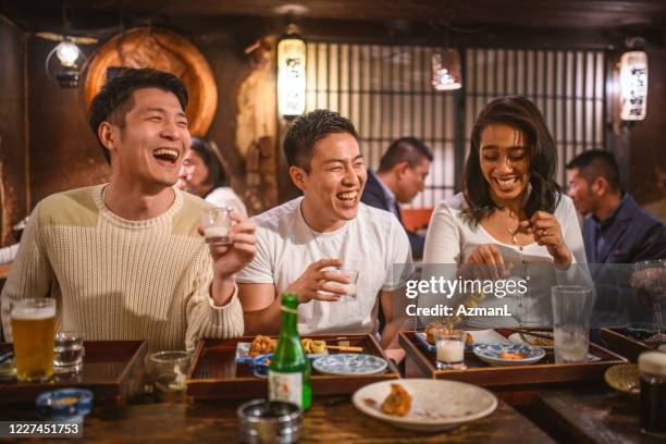 multi-ethnic friends drinking sake and laughing at izakaya - sake stock pictures, royalty-free photos & images