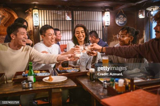 multi-ethnic group of friends toasting with sake at izakaya - izakaya imagens e fotografias de stock