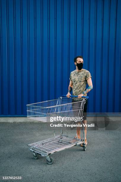 man in protective mask pushing shopping cart - shopping trolleys stockfoto's en -beelden