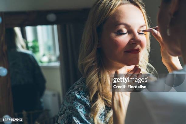 young girl doing eyelash extension to a beautiful blonde middle-aged woman - false eyelash stock-fotos und bilder