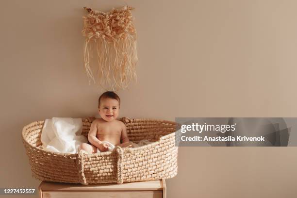 smiling baby sitting in moses basket.
6 month old baby sitting in basket bassinet under raffia macrame panno. baby eco nursery. - beige bedroom stock pictures, royalty-free photos & images