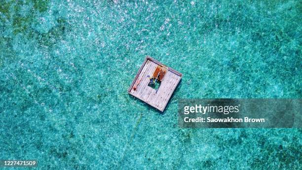 aerial view of young woman lying on wooden platform floating over crystal water, tied with rope on shore of tropical island in maldives - pontoon boat stock pictures, royalty-free photos & images
