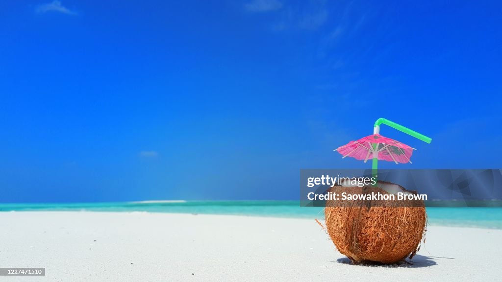 Coconut juice with pink parasol over white sand of tropical beach. summer concept. Copy space