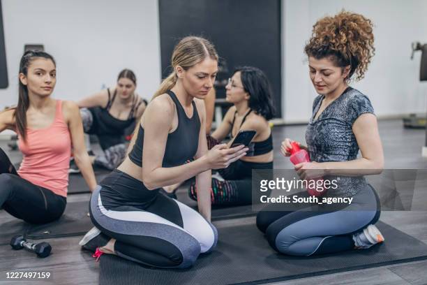 group of fitness women resting on the exercising mat and using smart phome - cell phome stock pictures, royalty-free photos & images