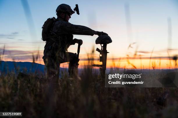 sad soldier kneeling for honoring his fallen friend - military memorial stock pictures, royalty-free photos & images