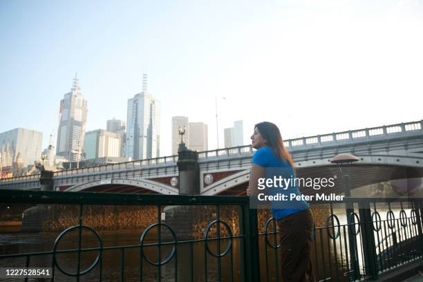 woman standing on yarra river promenade, melbourne skyline in background, australia. - melbourne skyline stock pictures, royalty-free photos & images