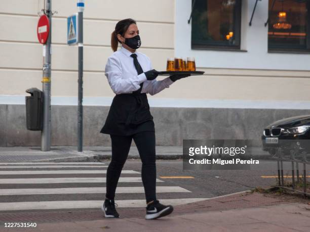 Waitress wearing a face mask crosses a pedestrian walk to serve beers at a terrace on May 27 ​ in the affluent​ neighborhood of Barrio de Salamanca...