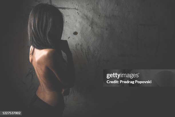 sad woman with hidden face over dark wall with space for text - human trafficking stockfoto's en -beelden