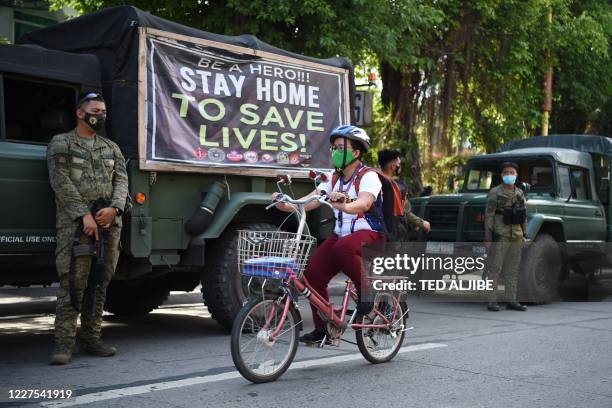 Resident rides her bicycle past armed soldiers along a street in Navotas in suburban Manila on July 16 after the local government reimposed a...