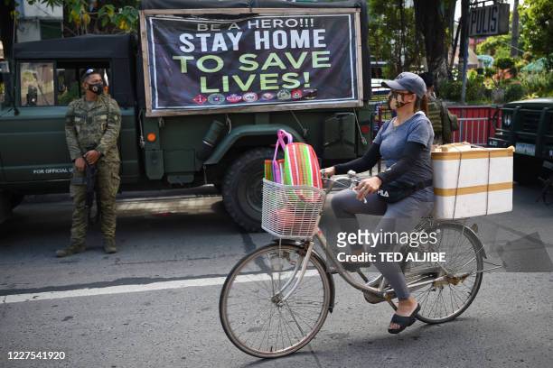 Resident rides her bicycle past armed soldiers along a street in Navotas in suburban Manila on July 16 after the local government reimposed a...