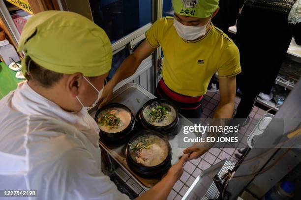 Staff member carries a tray of chicken and ginseng soup dishes known as 'samgyetang', at the Tosokchon Samgyetang restaurant in Seoul on July 16,...