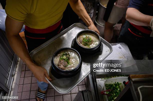 Staff member carries a tray of chicken and ginseng soup dishes known as 'samgyetang', at the Tosokchon Samgyetang restaurant in Seoul on July 16,...