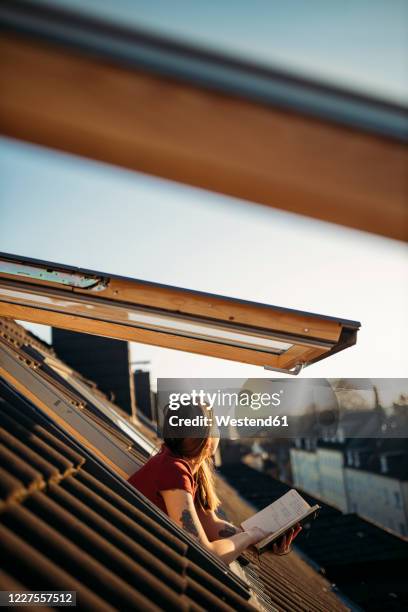 young woman with a book at the window looking out - blick durchs fenster aussenaufnahme haus stock-fotos und bilder