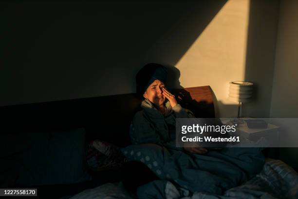 young woman with head wrapped in a towel lying in bed at home - rubbing eyes stockfoto's en -beelden