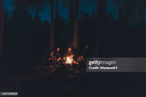 friends sitting at campfire in the woods - fogueira de acampamento imagens e fotografias de stock