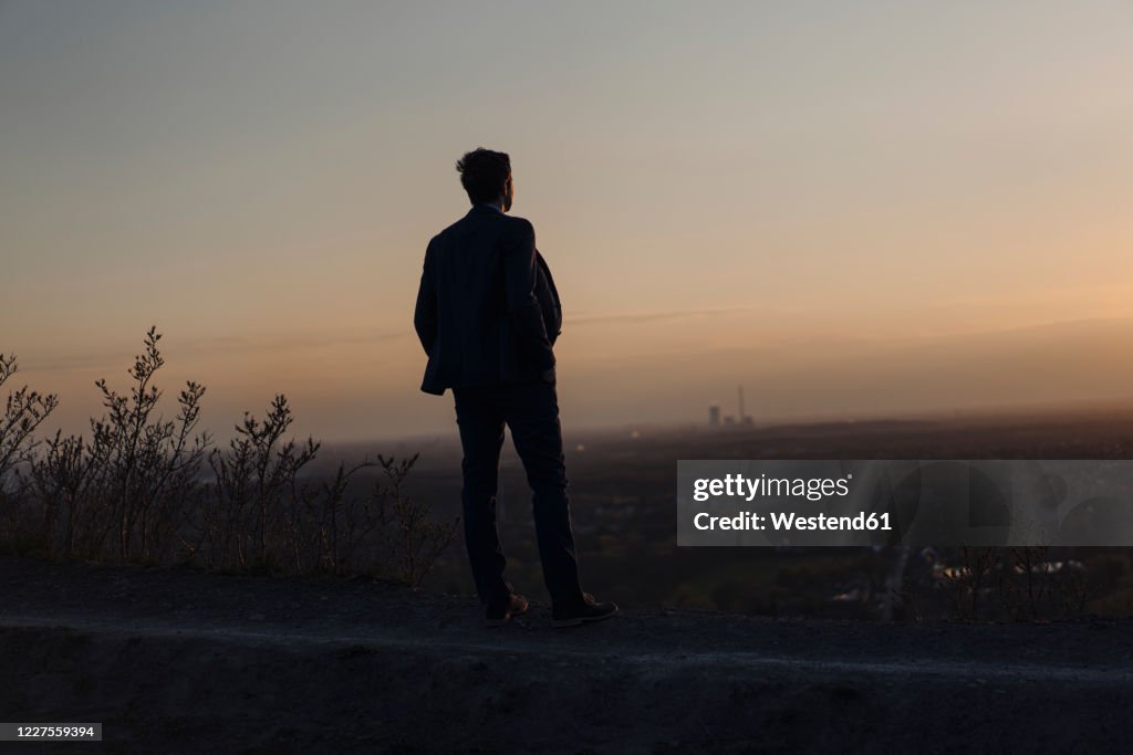 Mature businessman standing on a disused mine tip at sunset looking at view