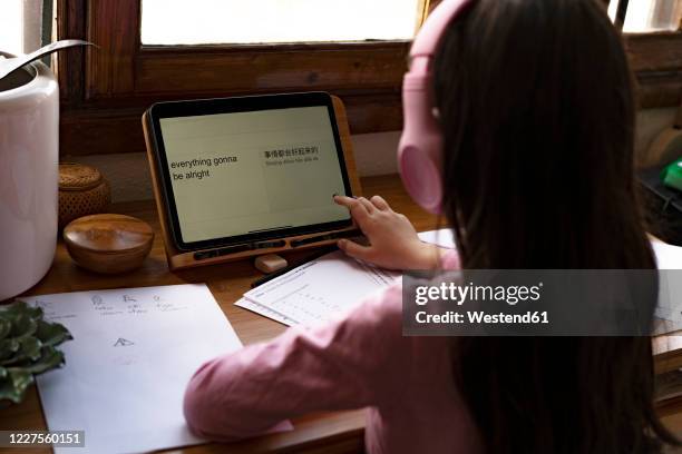 girl wearing headphones translating languages on digital tablet while learning comics at home - übersetzung stock-fotos und bilder